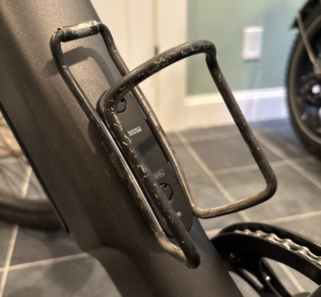 Image of a metal water bottle cage with a small plastic piece in the center.