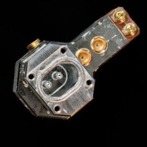 Image with a black background. There's a silver metal device in the foreground, with a large cavity at one end, containing two posts.