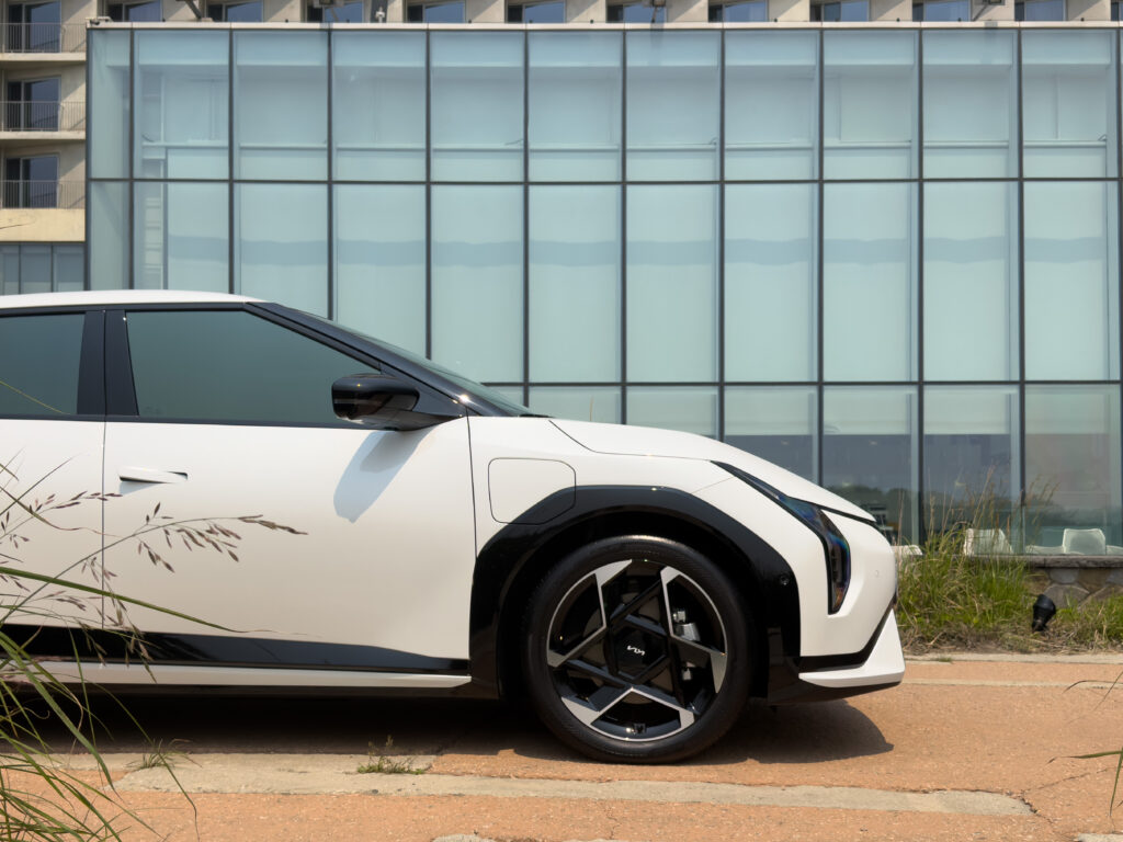 The front of a Kia EV4 in front of a brutalist window.