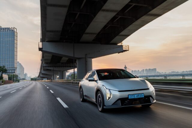 A Kia EV4 drives on a highway at dawn.