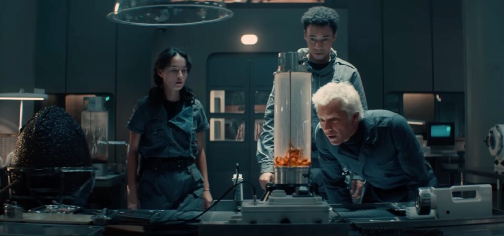 three people in a science lab looking at something gross in a transparent cylinder on the bench