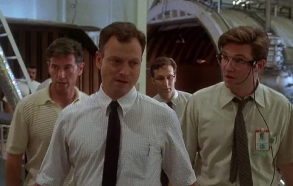 Group of men in dress shirts and ties walking near a testing module looking concerned.