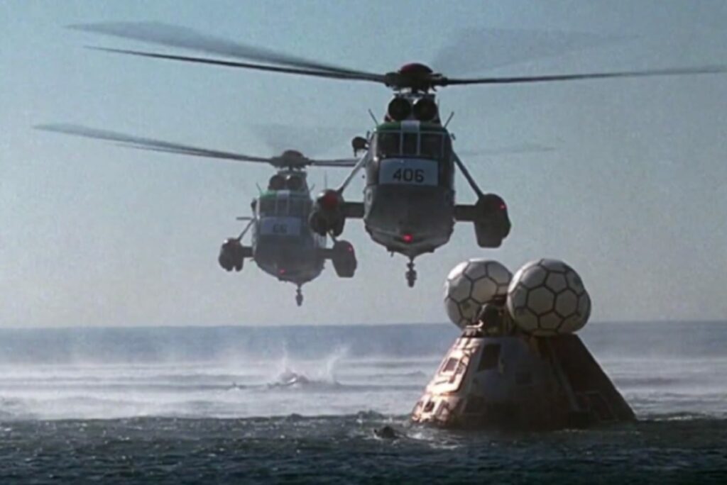 two helicopters flying over the ocean toward a floating space capsule