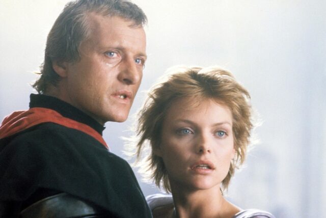 Handsome man in period dress standing close to a beautiful woman with short blonde hair, as they both look apprehensively into the distance.