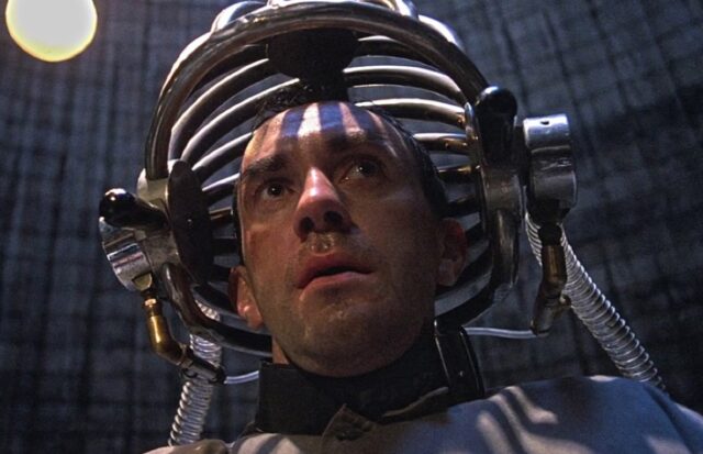 anxious man being restrained with his head in a weird futuristic helmet