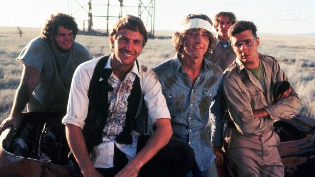 a group of young men in casual garb standing in a row in front of a car against a classic Americana small town background