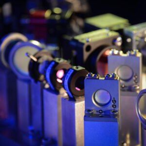 Image of a series of lenses held by vertical metal pillars. Other sets of lenses are behind these, and the background is black.