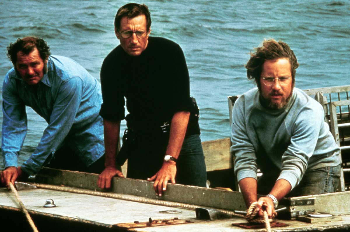 three men on a boat tossing chum into the water.