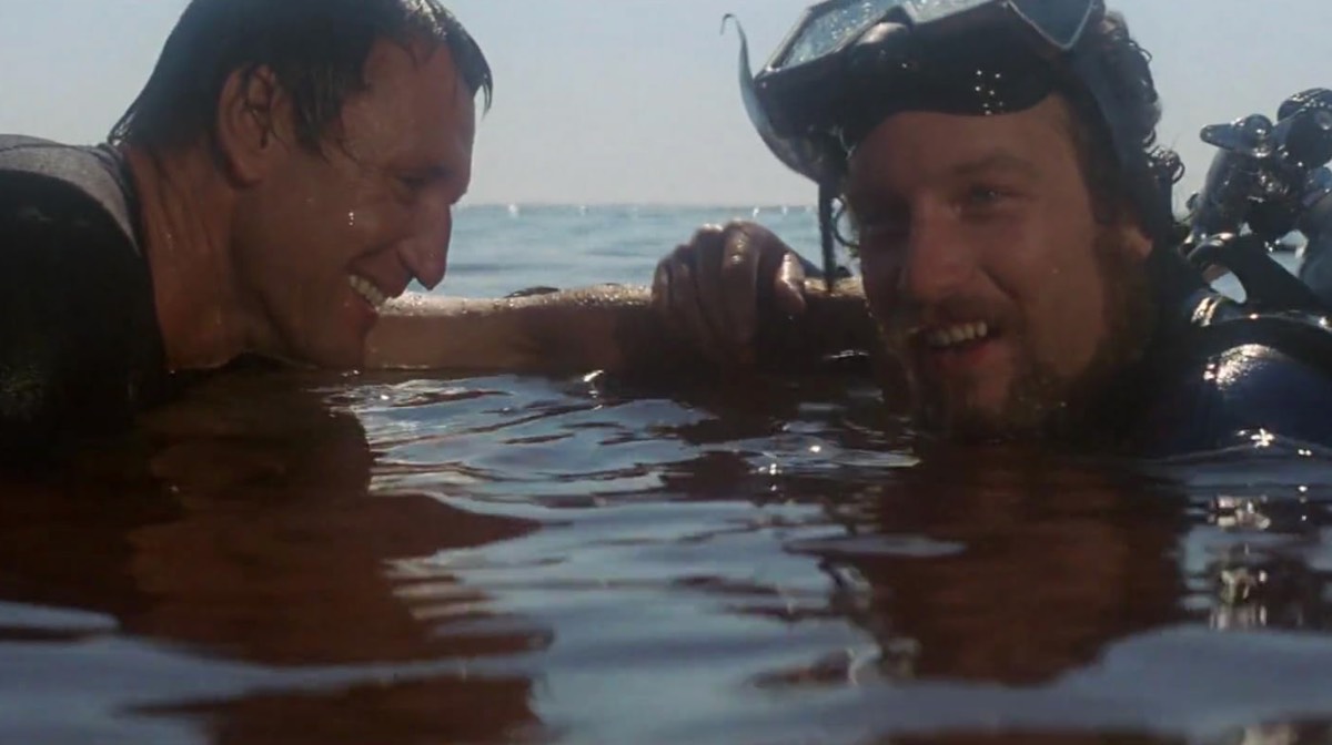two men in blood infused sea water smiling and laughing because the shark is dead