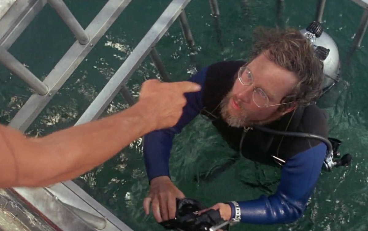 man with glasses and beard in scuba gear getting into a shark cage.