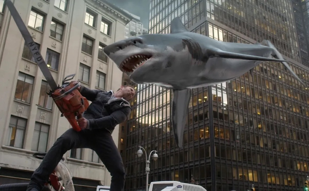 man wielding a chainsaw on a city street facing off against a shark flying at him through the air