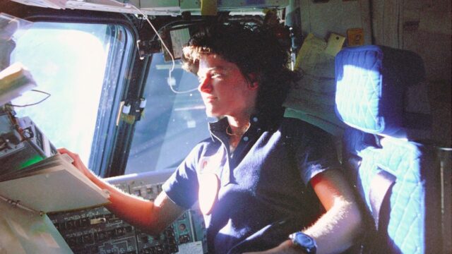 Sally Ride, mission specialist on STS-7, monitors control panels from the pilot's chair on the Flight Deck. Floating in front of her is a flight procedures notebook.