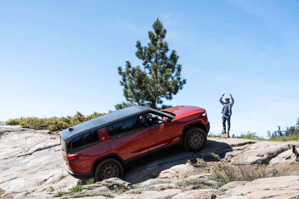 A red Rivian R1S being guided up a steep rock