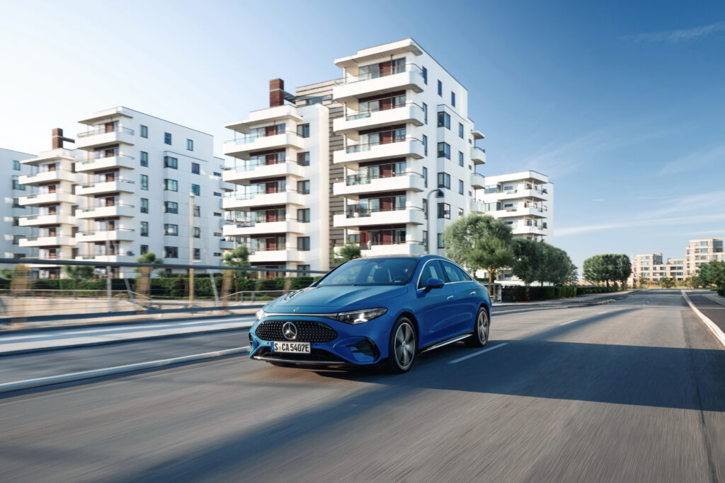 A blue Mercedes CLA drives towards the camera in a city