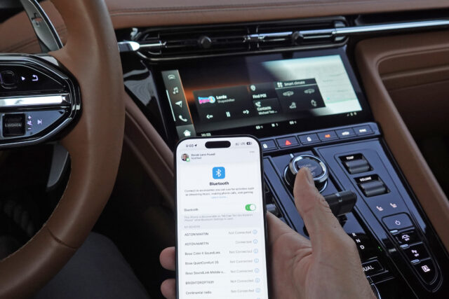 An iPhone next to an Aston Martin infotainment display