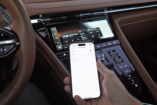 An iPhone next to an Aston Martin infotainment display