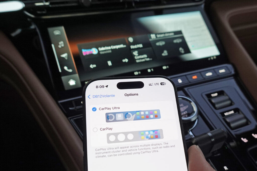 An iPhone next to an Aston Martin infotainment display