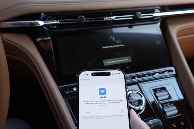 An iPhone next to an Aston Martin infotainment display
