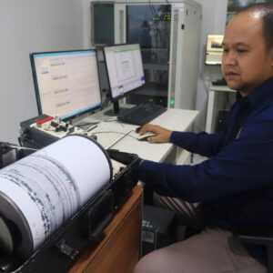 Image of a man in front of a computer, with a seismograph read out spooling across paper to his left.