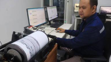 Image of a man in front of a computer, with a seismograph read out spooling across paper to his left.