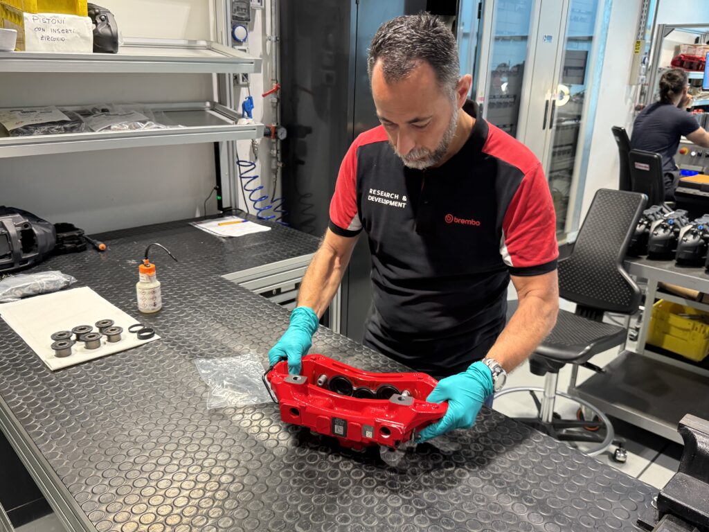 A Brembo technician handles a red-painted brake caliper.