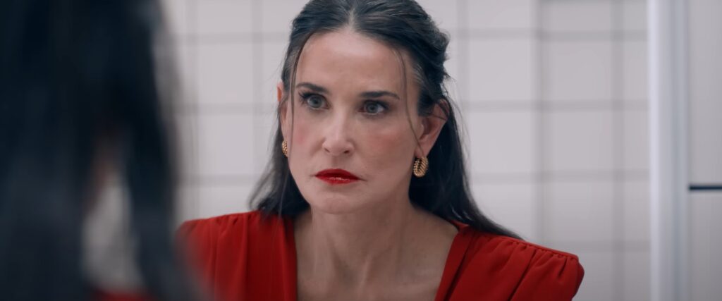 Demi Moore looking into a mirror and wearing a red dress and red lipstick in The Substance.