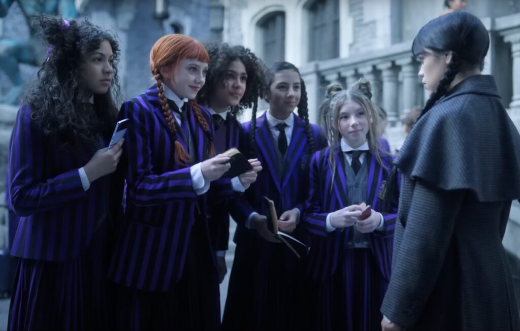 excited group of girls in school uniforms crowding around dark haired girl, autograph books in hands.
