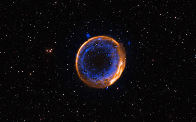 暗背景上点缀着星星，中心有一个明亮的环，由外层橙色和内层蓝色环组成。