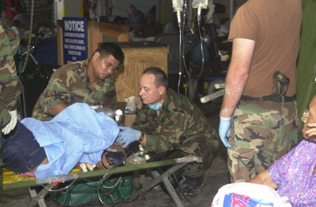 Two military personnel attend to an injured person on a cot in the Superdome.