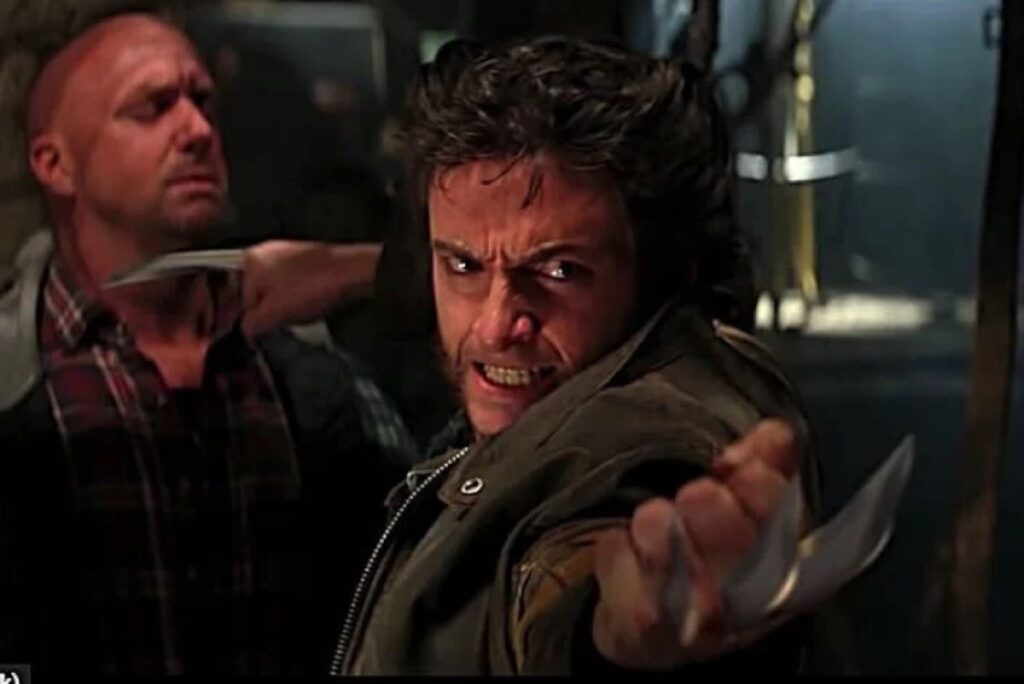 dark haired man with sideburns and claws coming out of his hands holds one against the throat of an attacked and points the other at a second attacker