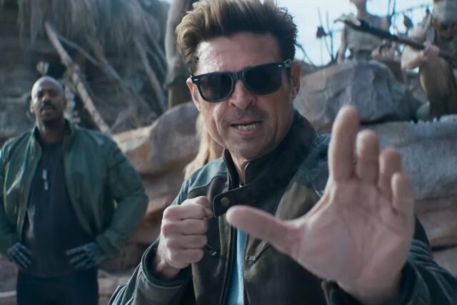 dark haired man in glasses and leather jacket raising his hands for a fight.