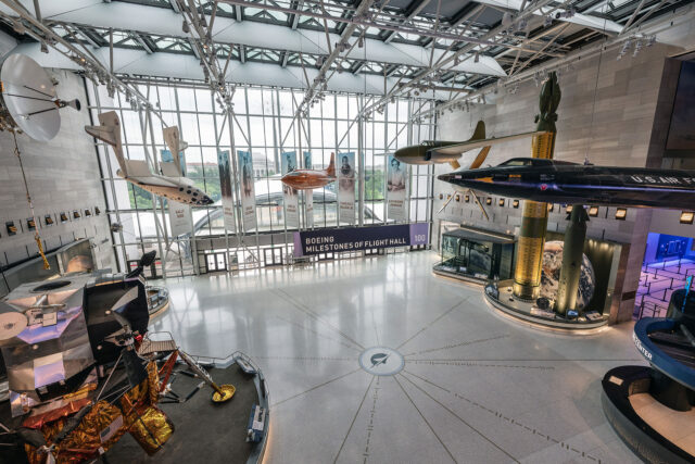 the view looking down and into a museum gallery with aircraft suspended from the ceiling, spacecraft on display and a binary map embedded in the flooring