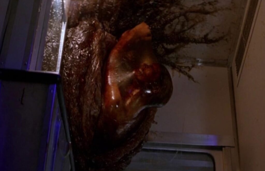 large gooey mass hanging in the corner of a train compartment with a human figure barely visible inside