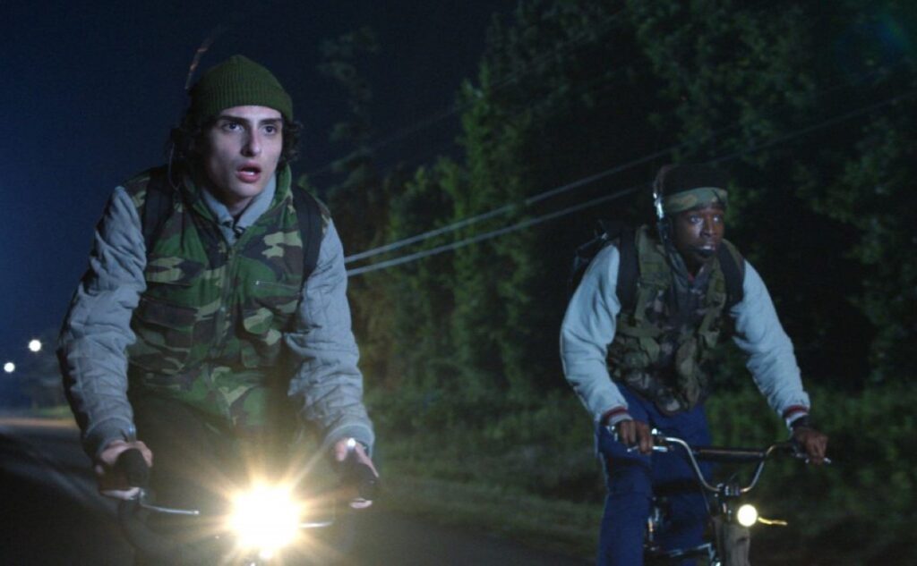 two young men riding bikes in a dark suburban street
