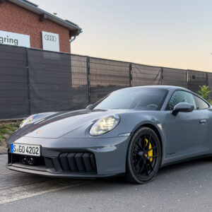 A grey Porsche 911 parked outside a building with an Audi logo and Nurburgring on the side.