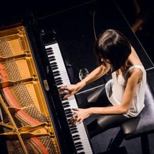 An overhead view of a woman with dark hair and a white top playing a concert piano.