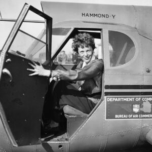 Amelia earhart in aviation garb sitting in cockpit of a plane
