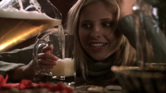 Young blonde woman smiling expectantly as someone pours her a glass of beer