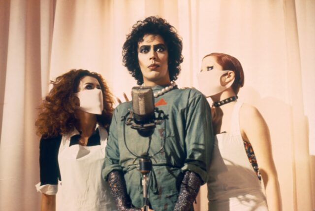 transvestite man in green doctor's coat with two women in nurse uniforms on either side