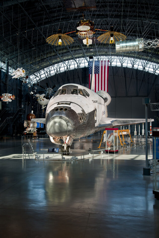 a space shuttle orbiter sits at the center of a hangar on display