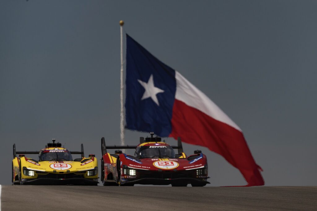 A pair of Ferrari 499Ps with a huge Texas flag in the background.
