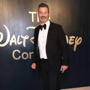 Jimmy Kimmel wearing a tuxedo and standing in front of a Walt Disney Company logo.