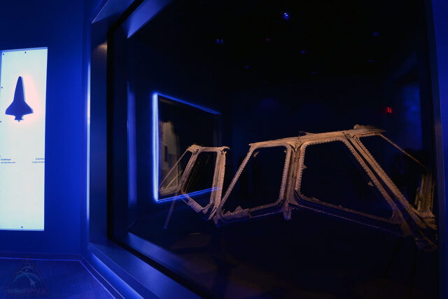 metal window frames are exhibited in a dark hall behind glass