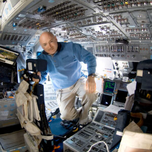 a man in a blue shirt and khaki slacks is seen surrounded by switches and displays aboard a spacecraft