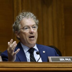 Senator Rand Paul sitting and holding his hands out at his sides while speaking during a committee hearing.
