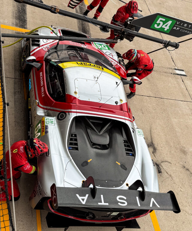 A Ferrari 296 GT3 race car during a pit stop, seen from above.