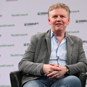 A man in a suit jacket sits at a TechCrunch speaking event