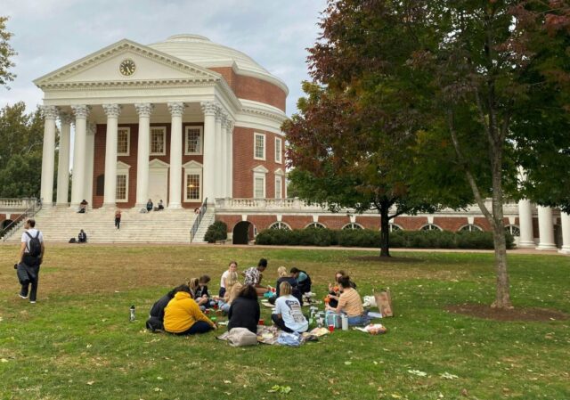 A large lawn dotted with students ends at the steps of a red brick building with a dome and classical colonnade.