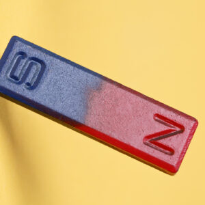 A yellow background with a bar magnet in the foreground, with the magnetic north painted red, and the magnetic south pained blue.
