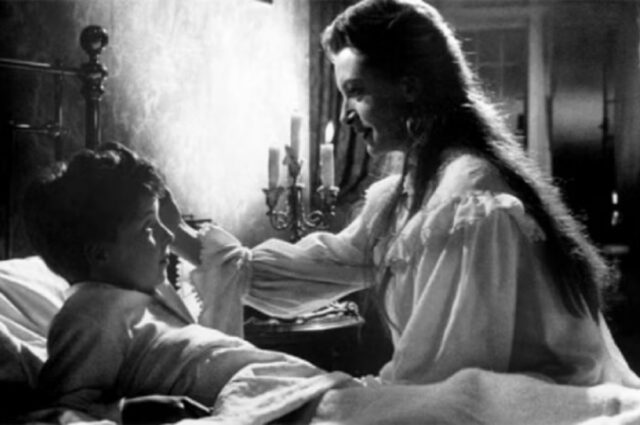 B&W still of young boy being tucked in by a young woman.